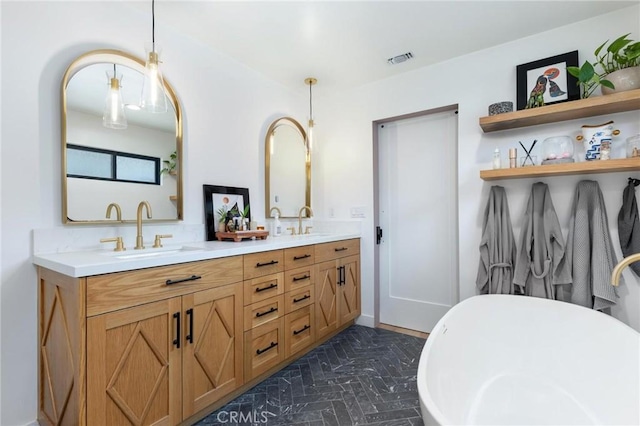 full bath featuring double vanity, visible vents, a freestanding tub, and a sink
