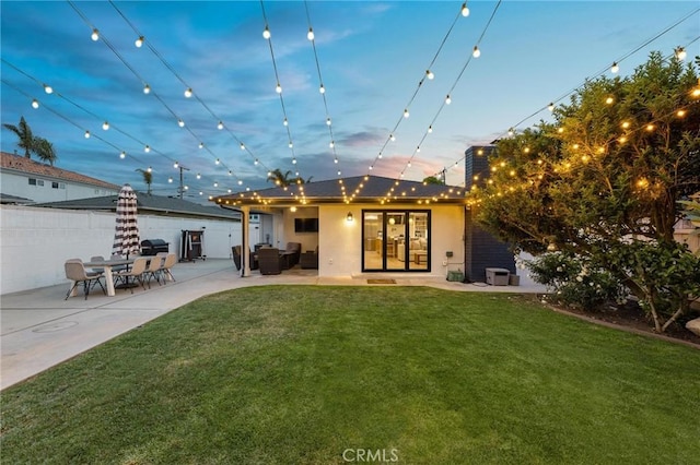 rear view of house with a yard, a patio area, stucco siding, and french doors