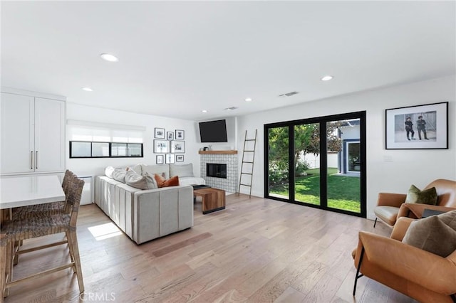 living room featuring a fireplace, light wood finished floors, visible vents, and recessed lighting