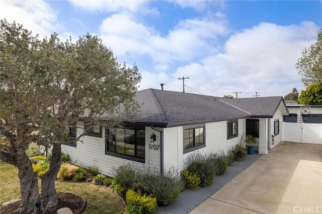 view of front of house featuring roof with shingles, concrete driveway, and fence