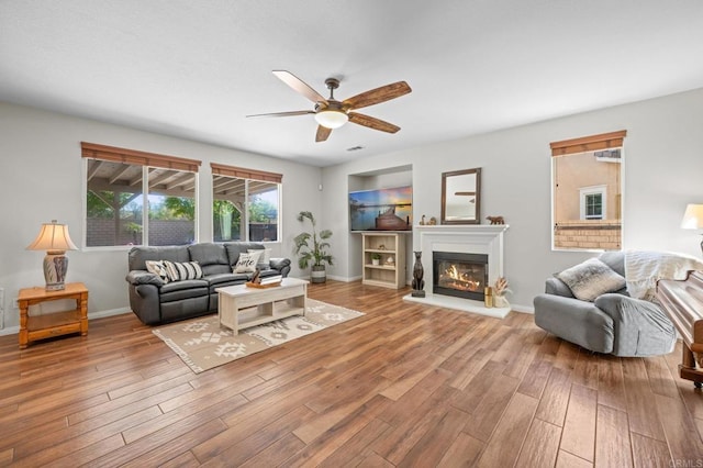 28829 Golden Dawn Dr, Menifee, CA 92584 - living area featuring a glass covered fireplace, baseboards, a ceiling fan, and wood finished floors