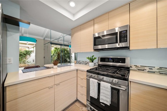 kitchen with a peninsula, light countertops, light brown cabinets, modern cabinets, and appliances with stainless steel finishes