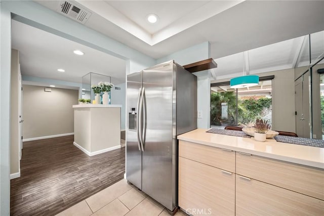 kitchen with stainless steel refrigerator with ice dispenser, visible vents, light wood finished floors, light countertops, and baseboards