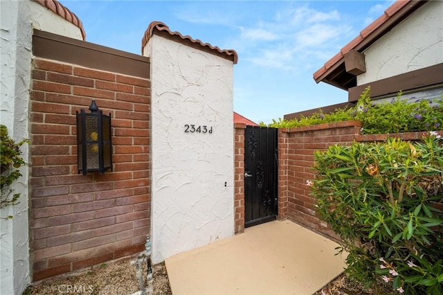 property entrance with brick siding, fence, and a gate