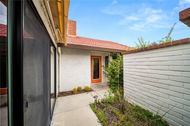 property entrance with stucco siding, a tiled roof, and fence