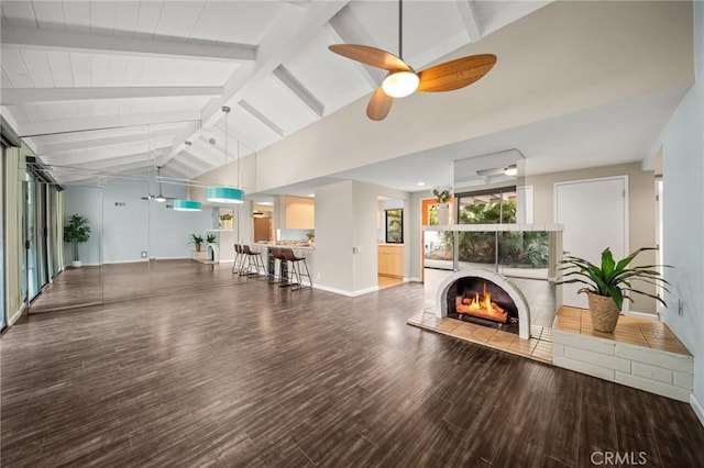 living room featuring wood finished floors, a ceiling fan, baseboards, a tiled fireplace, and vaulted ceiling with beams