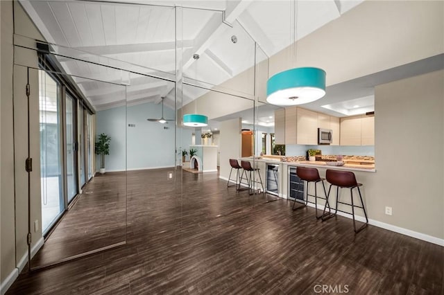 interior space featuring wood finished floors, a kitchen bar, lofted ceiling with beams, baseboards, and stainless steel microwave