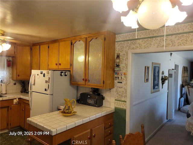 18340 Delicious St, Adelanto, CA 92301 - kitchen featuring freestanding refrigerator, decorative backsplash, a ceiling fan, wallpapered walls, and brown cabinets
