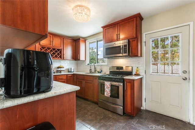 kitchen featuring a notable chandelier, a sink, brown cabinetry, stainless steel appliances, and tasteful backsplash