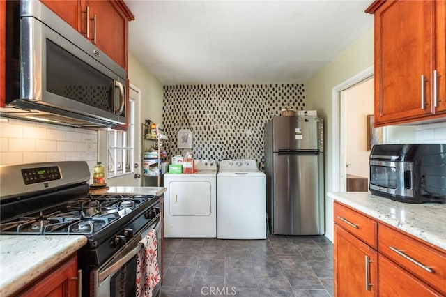 kitchen with brown cabinets, light stone countertops, appliances with stainless steel finishes, tasteful backsplash, and washing machine and dryer