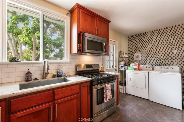 kitchen with decorative backsplash, light stone countertops, separate washer and dryer, a sink, and appliances with stainless steel finishes