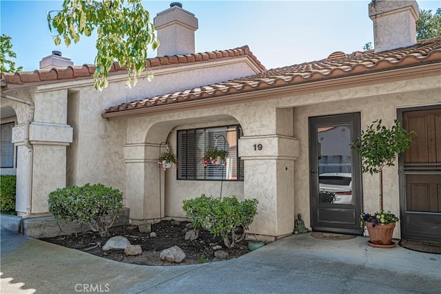 view of exterior entry featuring a chimney and stucco siding