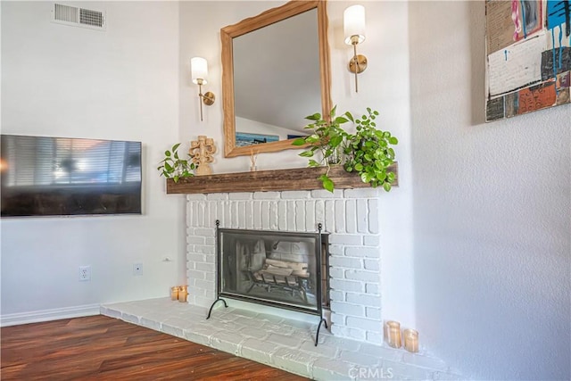 interior details featuring visible vents, baseboards, a brick fireplace, and wood finished floors