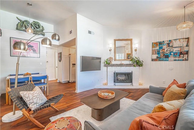 living area featuring a brick fireplace, baseboards, visible vents, and wood finished floors