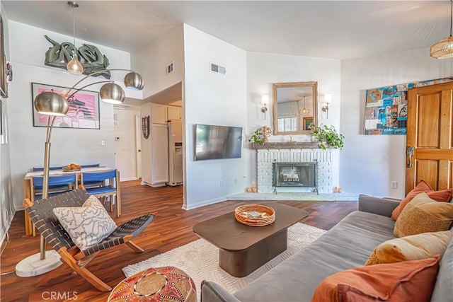 living area featuring a brick fireplace, baseboards, visible vents, and wood finished floors