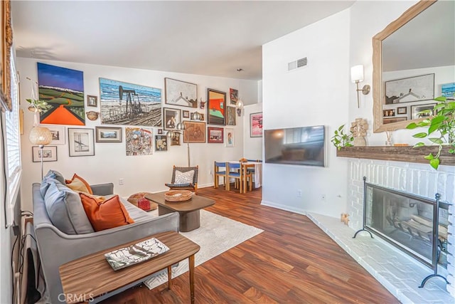 living area featuring a brick fireplace, wood finished floors, and visible vents