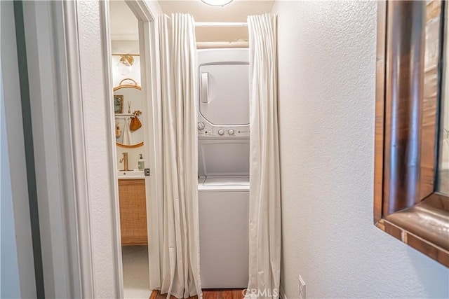 clothes washing area featuring laundry area, a textured wall, and stacked washer / dryer