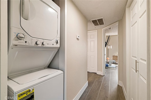 washroom with visible vents, baseboards, stacked washing maching and dryer, a textured ceiling, and dark wood finished floors