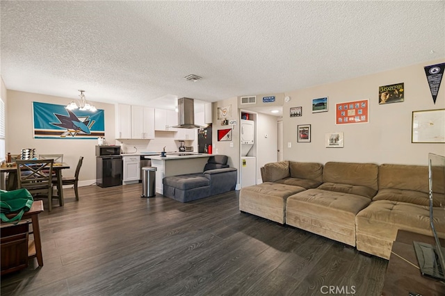 living room featuring a textured ceiling, stacked washer / drying machine, a notable chandelier, and dark wood-type flooring
