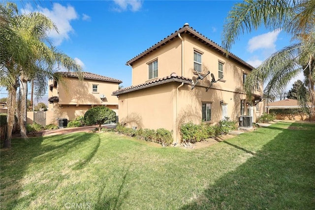 back of property featuring a yard, a tiled roof, central AC unit, and stucco siding