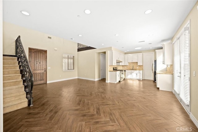unfurnished living room featuring a sink, baseboards, plenty of natural light, and visible vents