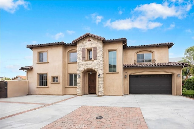 mediterranean / spanish-style home with a tile roof, a garage, concrete driveway, stone siding, and stucco siding