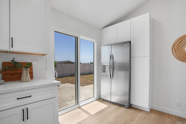 interior space featuring baseboards, light wood-type flooring, and lofted ceiling