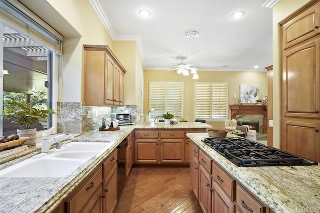 kitchen featuring a ceiling fan, crown molding, a sink, black appliances, and a warm lit fireplace