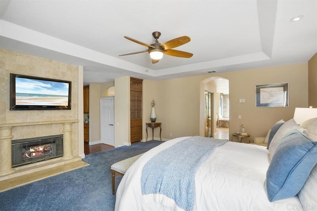 bedroom with a premium fireplace, arched walkways, a tray ceiling, and ensuite bath