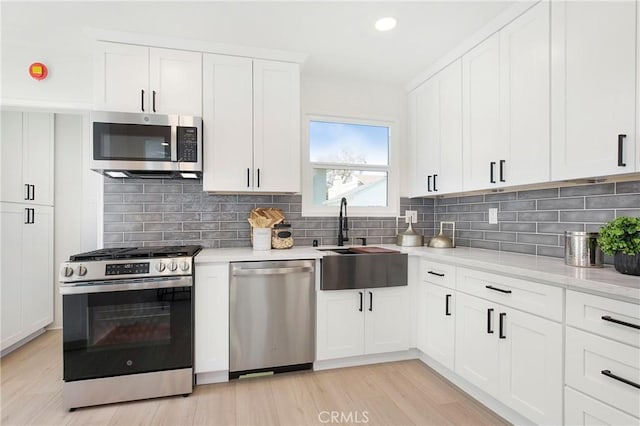 kitchen featuring tasteful backsplash, a sink, white cabinets, stainless steel appliances, and recessed lighting