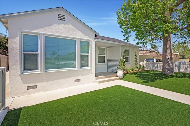 view of front facade with a front lawn, stucco siding, and fence