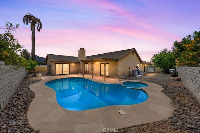 pool at dusk with a fenced backyard, a patio area, central AC, and a pool with connected hot tub
