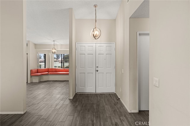 foyer featuring baseboards, dark wood-style flooring, a textured ceiling, and a chandelier
