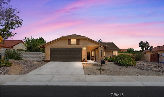ranch-style house featuring a garage, fence, stucco siding, and concrete driveway