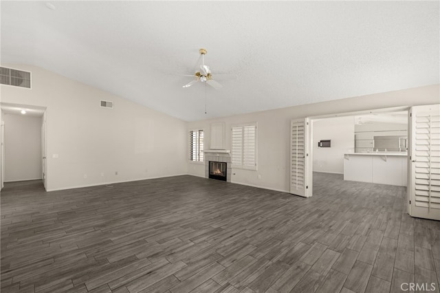 unfurnished living room featuring ceiling fan, dark wood finished floors, a tiled fireplace, lofted ceiling, and visible vents