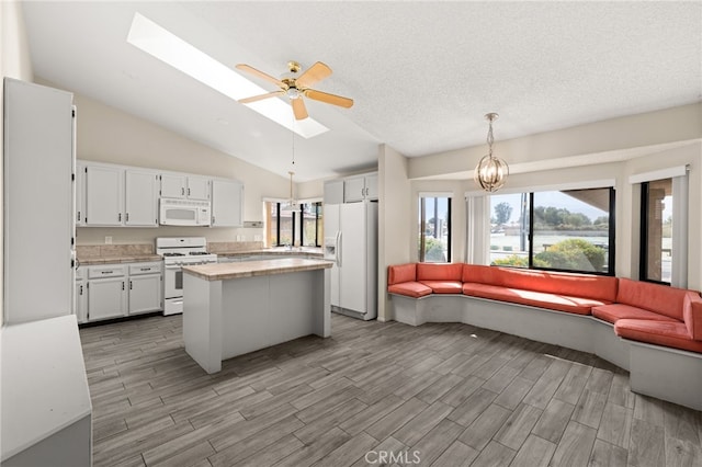 kitchen with vaulted ceiling with skylight, white appliances, light countertops, white cabinetry, and open floor plan
