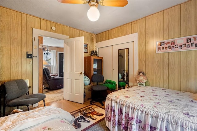 bedroom with a closet, a ceiling fan, wooden walls, and light wood-type flooring