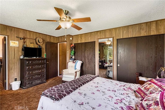 bedroom featuring wooden walls, a textured ceiling, carpet flooring, and two closets