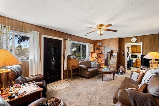 living area with wooden walls, a ceiling fan, visible vents, and light carpet