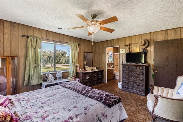 bedroom with a textured ceiling, wood walls, dark carpet, and visible vents