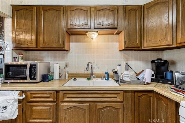 kitchen featuring brown cabinets, a sink, light countertops, stainless steel microwave, and decorative backsplash