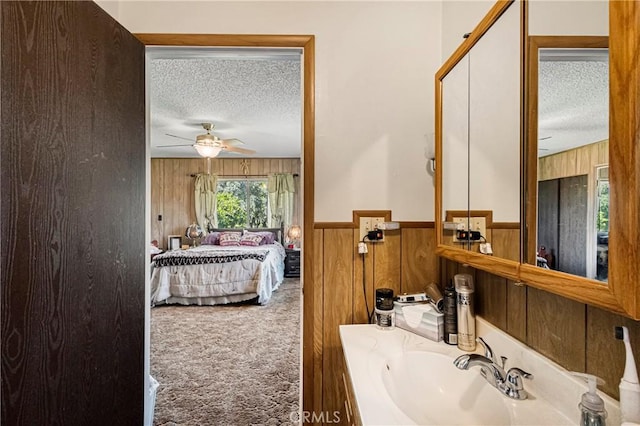 bathroom featuring a ceiling fan, a textured ceiling, wood walls, a sink, and ensuite bathroom