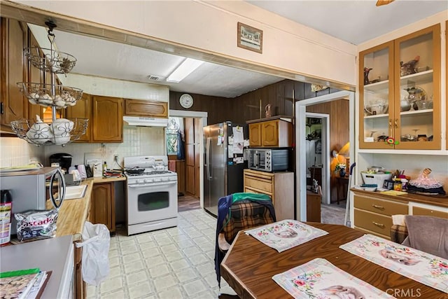 kitchen featuring light floors, light countertops, under cabinet range hood, appliances with stainless steel finishes, and backsplash