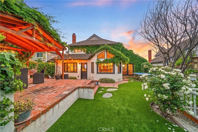 28102 Camellia Ct, Laguna Niguel, CA 92677 - back of property at dusk featuring central air condition unit, stucco siding, a chimney, a lawn, and a patio