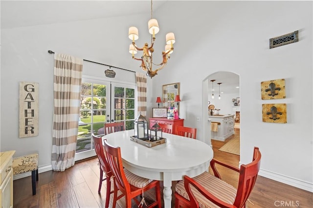 dining area with arched walkways, high vaulted ceiling, a chandelier, wood finished floors, and visible vents