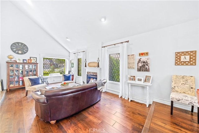 living area featuring a warm lit fireplace, baseboards, high vaulted ceiling, and hardwood / wood-style floors