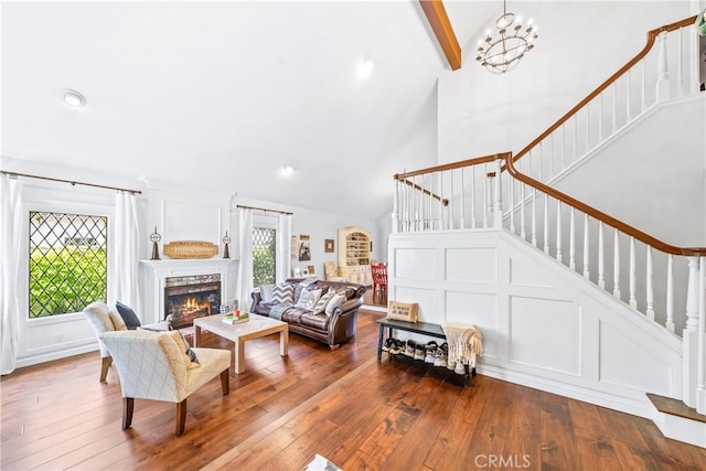 living room featuring high vaulted ceiling, dark wood-style flooring, a lit fireplace, and stairs