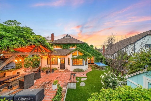 back of property at dusk with an outdoor hangout area, a patio, stucco siding, and a yard
