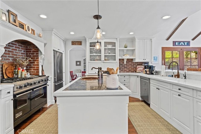 kitchen featuring stainless steel appliances, open shelves, an island with sink, and a sink
