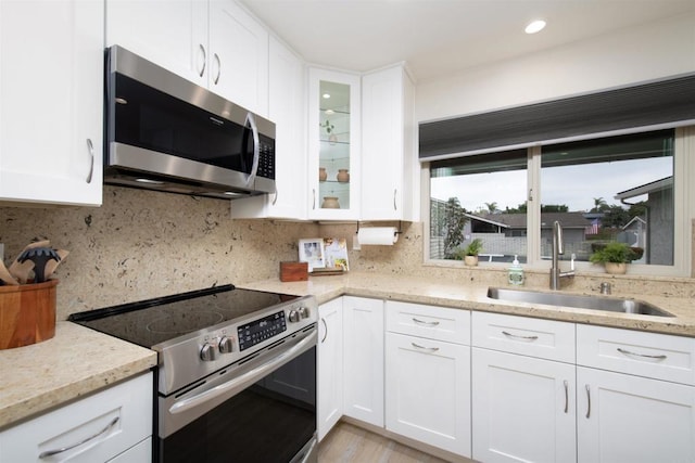 kitchen featuring light stone countertops, glass insert cabinets, white cabinetry, a sink, and appliances with stainless steel finishes